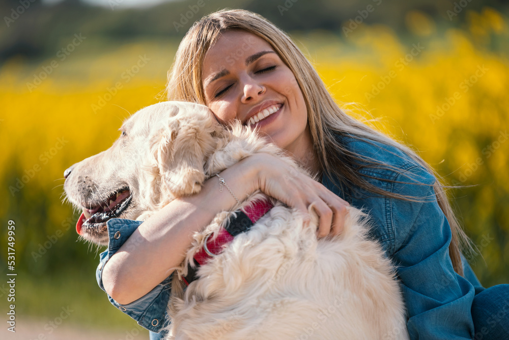Attractive young woman caring and playing with her beautiful golden retriever dog in a rapessed fiel.