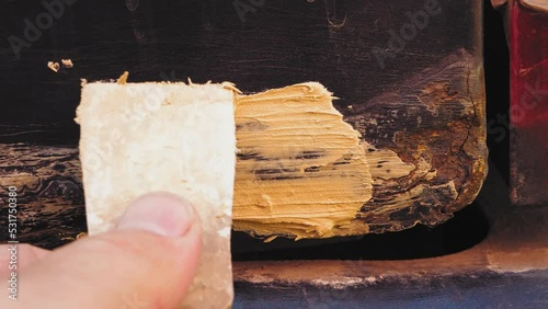 A man's hand with a spatula applies putty on a rusty fender of a car. Medium plan photo