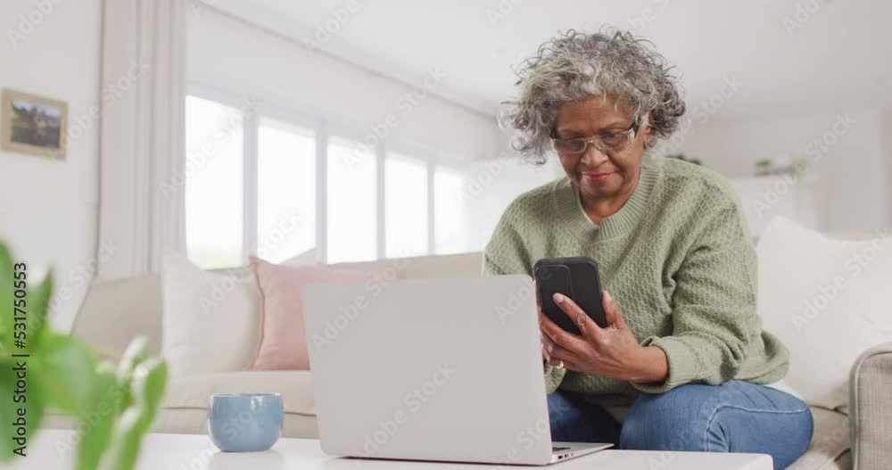 Portrait of happy senior african american woman sitting on sofa, using laptop and smartphone Portrait of happy senior african american woman sitting on sofa, using laptop and smartphone