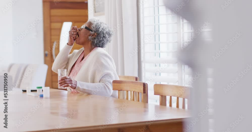 Senior african american woman sitting at table, taking pills Senior african american woman sitting at table, taking pills