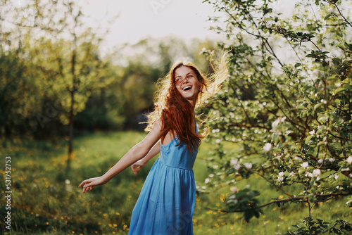 Woman with a beautiful smile with teeth and long hair flying hair spring dance hands up in the sunset in the park near the flowering trees happiness  natural beauty and hair health