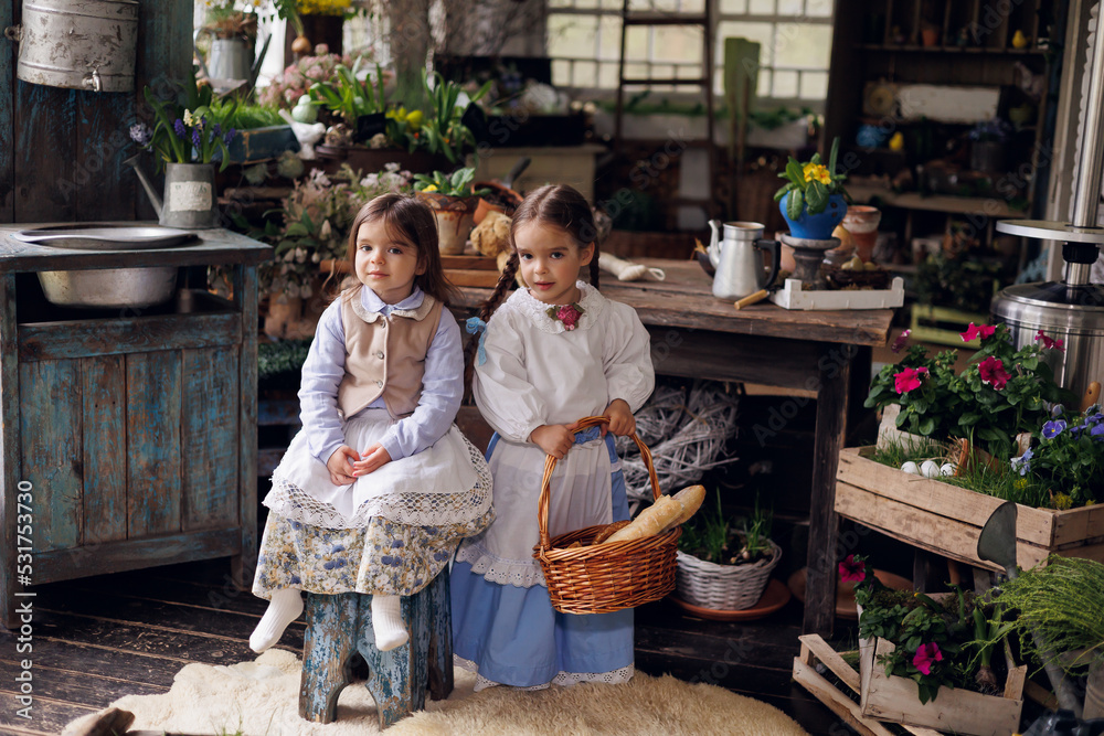 Two little girls sitting on terrace with basket of bread and buns. Little baby sisters of 3 and 5 in retro vintage dress having fun and smiling.