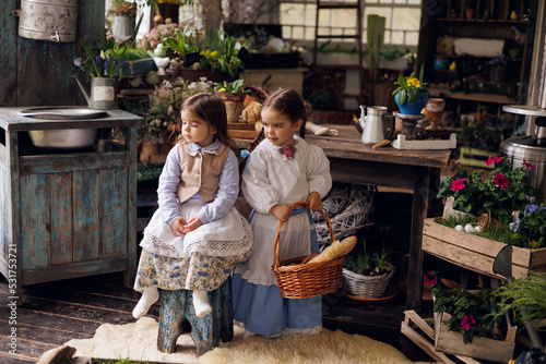 Two little girls sitting on terrace with basket of bread and buns. Little baby sisters of 3 and 5 in retro vintage dress having fun and smiling.