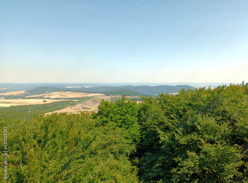 Hügelige Landschaft in der Vulkaneifel und der Laacher See im Hintergrund: Aussicht vom Sendeturm auf dem Berg Gänsehals bei Rieden im Landkreis Mayen-Koblenz, Rheinland-Pfalz.