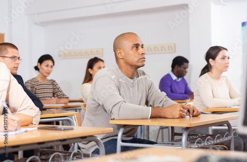 Concentrated hispanic man attentively listening and making notes of lecture during adult education class