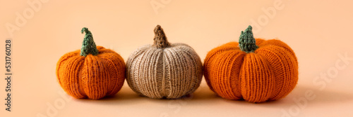 Knitted orange and beige pumpkins on an orange background, autumn composition, banner. Halloween concept.