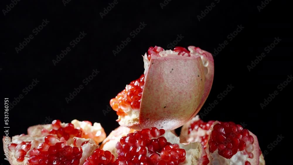 The pomegranate fruit, divided into parts, rotates against the background of pieces with red grains, on a black background. The pomegranate fruit, divided into parts, rotates against the background of pieces with red grains, on a black background.