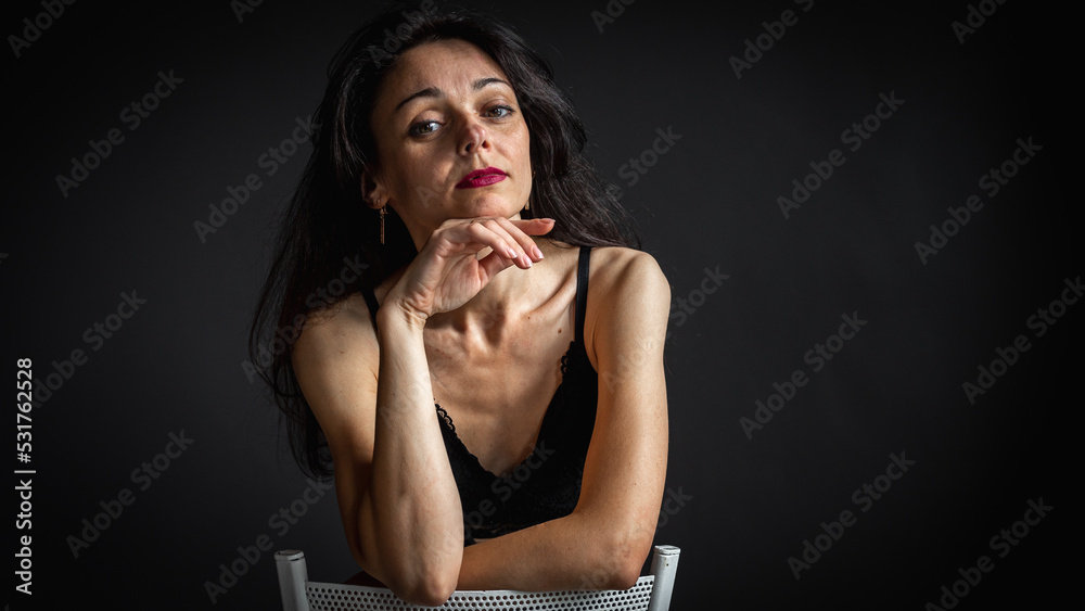 Full body photo of cute and seductive brunette woman sitting in pants on chair isolated on dark background Full body photo of cute and seductive brunette woman sitting in pants on chair isolated on dark background