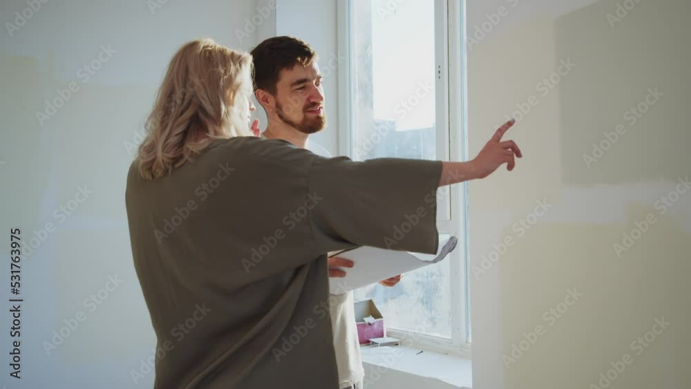 Beautiful couple young man and pregnant woman talking hold paper with visual repair. Happy family own new apartment. Home. Mortgage investment concept Beautiful couple young man and pregnant woman talking hold paper with visual repair. Happy family own new apartment. Home. Mortgage investment concept