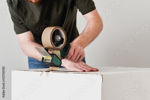 Detalle de un hombre usando una herramienta para precintar una caja de cartón con cinta adhesiva marrón. Embalaje de cajas de mudanza.