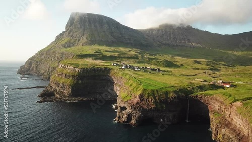 Aerial drone view of Mulafossur waterfall, Faroe Islands. Small village Gasadalur with a Hvannadalur valley and Arnafjall mountain hidden in a fog. Sunny day in summer. High quality 4k footage. photo