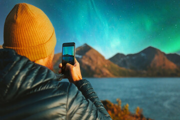Man with smartphone taking photo of northern lights winter travel in Norway adventure vacations outdoor blogger influencer lifestyle modern online technology