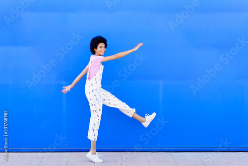 Cheerful black woman raising leg near wall