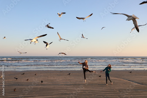 Two girls feeding flying seagulls on the beach