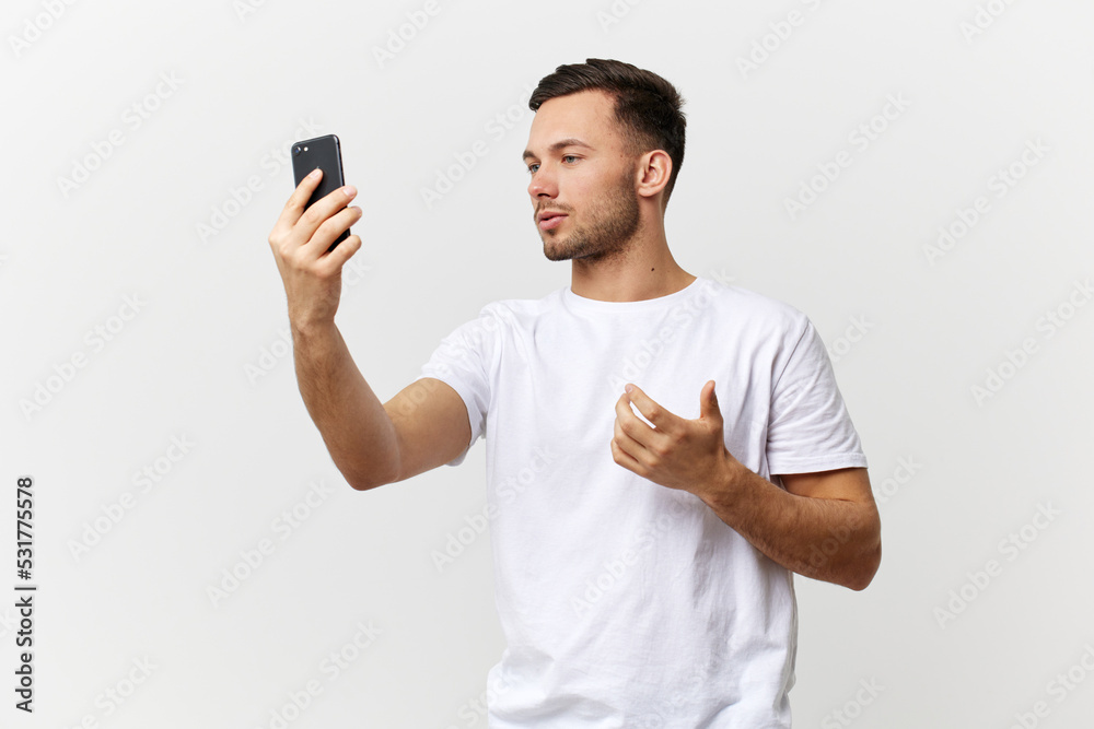 Concentrated handsome speaker influencer blogger man in basic t-shirt record live with phone posing isolated on white studio background. Copy space Banner Mockup. Distance online communication concept Concentrated handsome speaker influencer blogger man in basic t-shirt record live with phone posing isolated on white studio background. Copy space Banner Mockup. Distance online communication concept