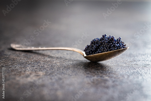 Black caviar in silver spoon on dark table.