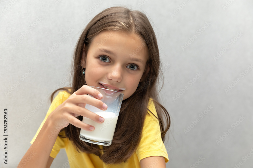 Cute little girl enjoying a glass of milk and smiling on a gray background Cute little girl enjoying a glass of milk and smiling on a gray background