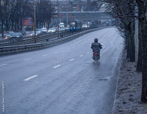 food delivery courier rides a motorcycle with a black thermal bag for delivering food in the rain along an empty road