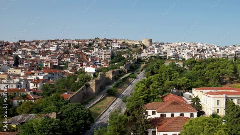 Aerial view of Thessaloniki on a sunny day. White buildings and the fortress drone shot. Flyover rooftops with sea in the background. Travel destination rich with history. Summer day in the city Aerial view of Thessaloniki on a sunny day. White buildings and the fortress drone shot. Flyover rooftops with sea in the background. Travel destination rich with history. Summer day in the city