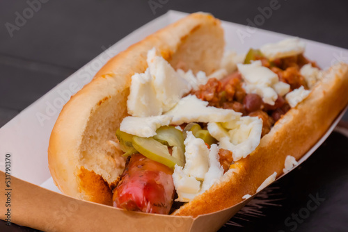 Sandwich, hot dog with sausage, cheese and sause ketchup in paper box on table at street food festival - close up. Outdoor cooking, gastronomy, takeaway food concept