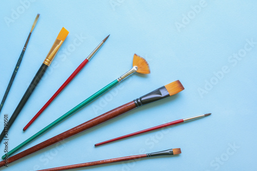 Various types of artistic paintbrushes on blue paper background. Copy space