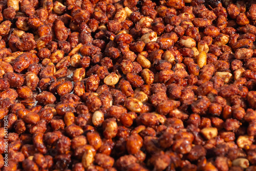 Heap of roasted caramelized sugared peanuts with warm and contrast sunlight illumination at summer outdoor food market - close up. Cookery, dessert, gastronomy and street food concept