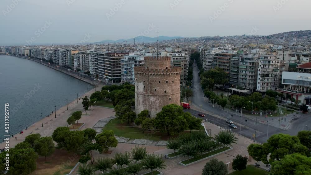 Aerial view of Thessaloniki White Tower at sunrise. Drone shot with soft morning light. Major city of Greece on the sea. Historical monument next to the boardwalk on the waterfront. Aerial view of Thessaloniki White Tower at sunrise. Drone shot with soft morning light. Major city of Greece on the sea. Historical monument next to the boardwalk on the waterfront.