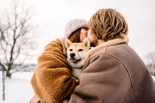 Cute young couple having fun in the winter park with their dog on bright day.Man and woman are relaxing