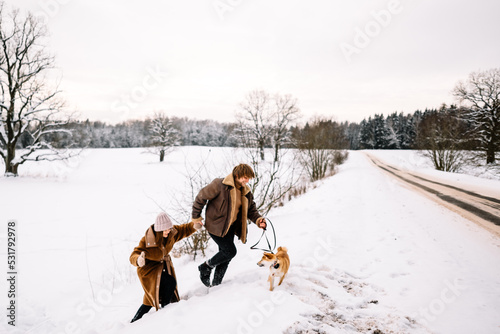 Fototapeta Naklejka Na Ścianę i Meble -  Cute young couple having fun in the winter park with their dog on bright day.Man and woman are relaxing