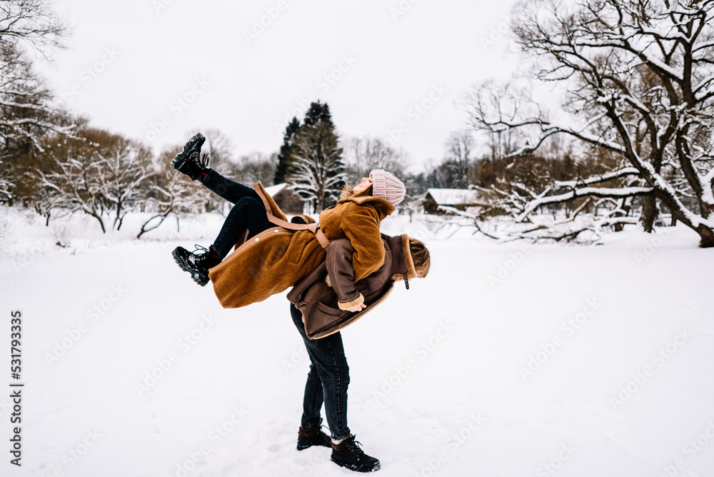Cute young couple in love having fun in the winter park on bright day. Woman and man relaxing outdoors