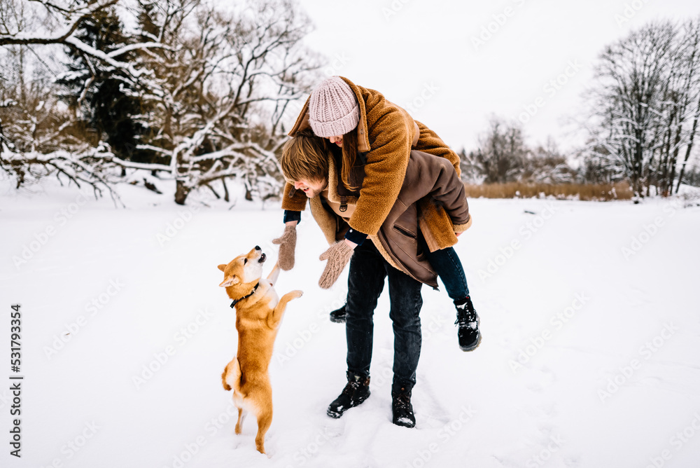 Cute young couple having fun in the winter park with their dog on bright day.Man and woman are relaxing Cute young couple having fun in the winter park with their dog on bright day.Man and woman are relaxing