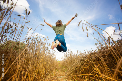 happiness, nature, summer holidays, recreation and the concept of people - a happy young woman jumping on a grain field