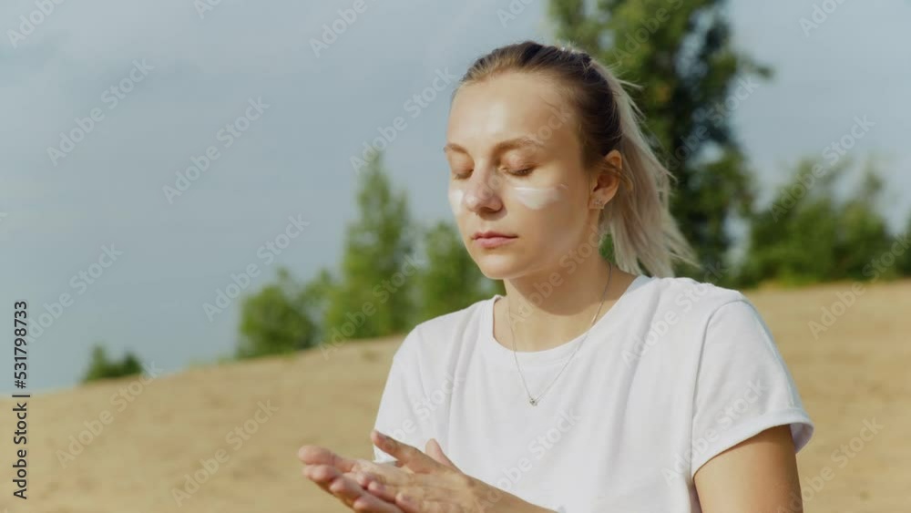 A young woman is sitting on the beach and smearing herself with sunscreen. Rest A young woman is sitting on the beach and smearing herself with sunscreen. Rest