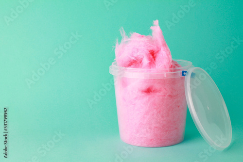close up sweet fluffy pink color cotton candy in plastic basket package on green background. spun sugar. minimal sweet concept. space for text, copy space