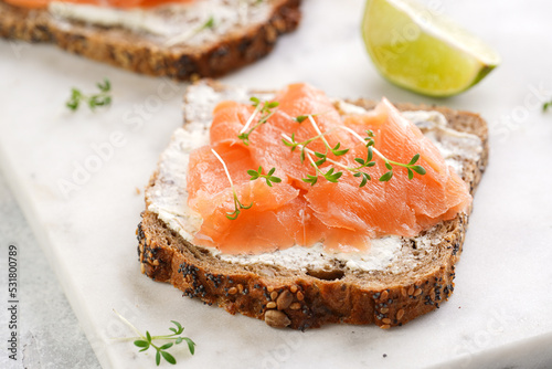 Wholewheat bread sandwiches with cream cheese and smoked salmon on marble board with lime slices and sour cream