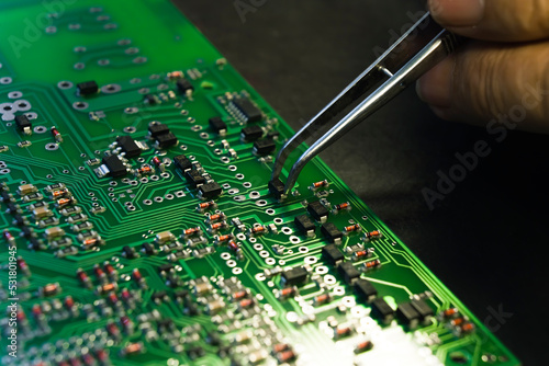 Close up shot of hand holding tweezers mounting electrical components onto PCB printed circuit board. Repairing electronics. Precise work. Horizontal shot. High quality photo