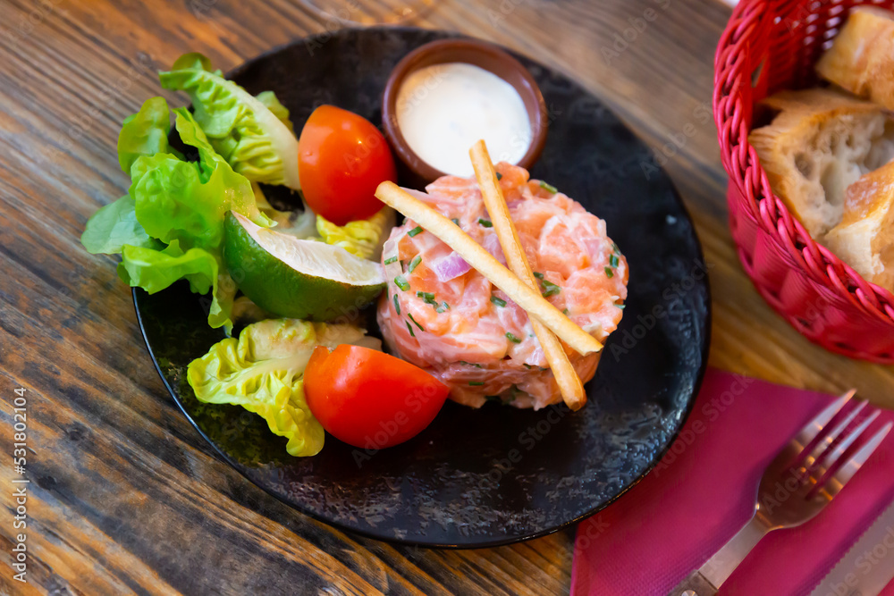 Popular appetizer of French cuisine is salmon tartare with onion cream, served with sliced tomato, lime, lettuce and sauce