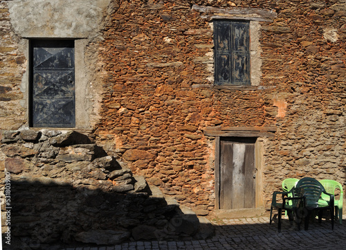 Parte de uma fachada de ruínas de uma casa velha de uma aldeia com cadeiras e mesa de plástico ao lado photo