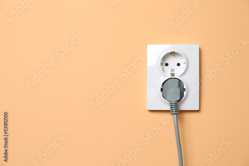 Double power socket with inserted plug on pale orange wall, space for text. Electrical supply
