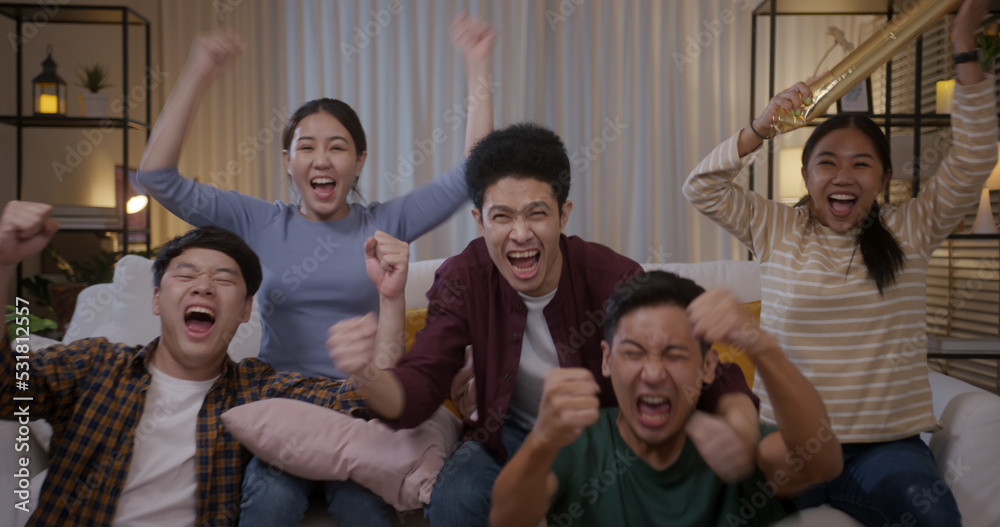 Fototapeta premium Group of young adult friend man and woman asia people sit at sofa couch joy night party fun game FIFA world cup live TV at home eat snack bowl drink beer bottle glass jump mad happy win exult face