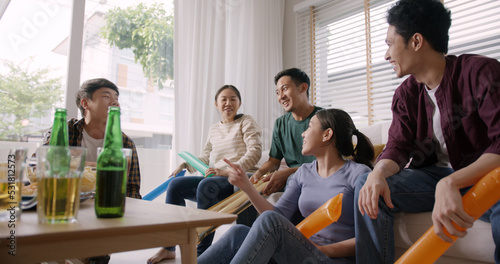 Group of young adult friend man and woman asia people sit at sofa couch joy chanting party fun game FIFA world cup live TV at home eat snack bowl drink beer bottle glass jump mad happy win exult face. photo