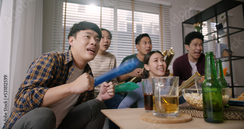 Group of young adult friend man and woman asia people sit at sofa couch joy chanting party fun game FIFA world cup live TV at home eat snack bowl drink beer bottle glass jump mad happy win exult face.