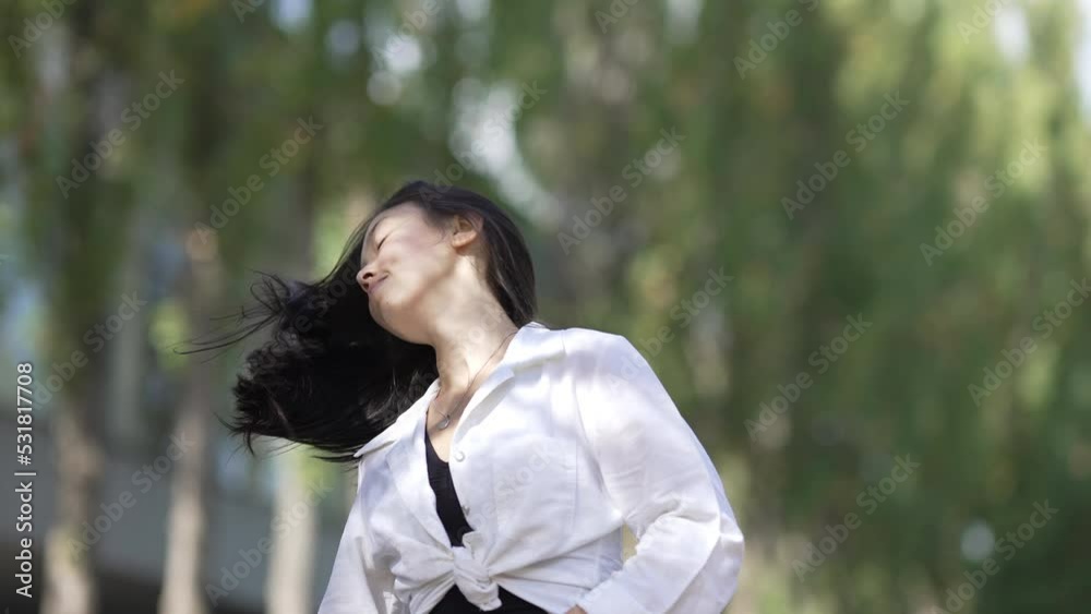 Gorgeous confident Asian slim woman tossing long black hair in slow motion looking at camera. Portrait of beautiful young lady posing in sunny summer park outdoors. Femininity and beauty Gorgeous confident Asian slim woman tossing long black hair in slow motion looking at camera. Portrait of beautiful young lady posing in sunny summer park outdoors. Femininity and beauty