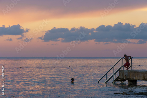 Two children swimming from a concrete pier just after sunset in Cozumel