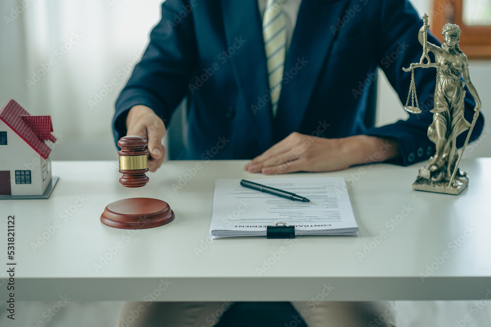Hand of a judge holding a hammer and a house model mediating property disputes in court or property auctioneers with the god of justice on the table. Hand of a judge holding a hammer and a house model mediating property disputes in court or property auctioneers with the god of justice on the table.