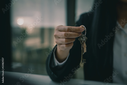 Real estate agents and sales representatives hand out keys from new homes to office clients with examples of homes laid out in front.