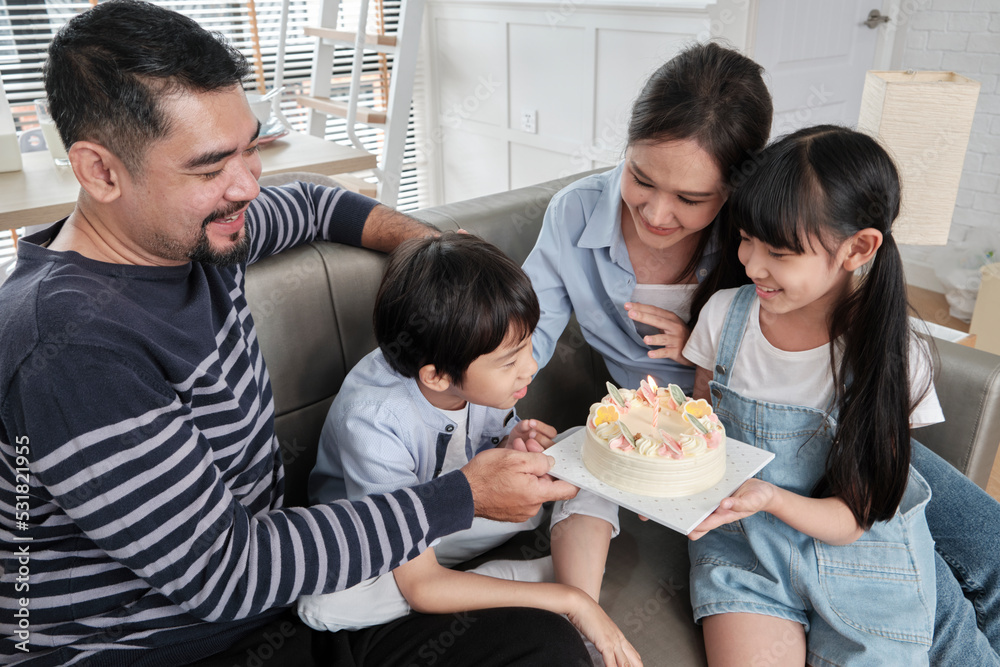 Happy Asian Thai family, young son is surprised with birthday cake, blows out candle, and celebrates joy party with parents and sister in living room together, wellbeing domestic home special event. Happy Asian Thai family, young son is surprised with birthday cake, blows out candle, and celebrates joy party with parents and sister in living room together, wellbeing domestic home special event.