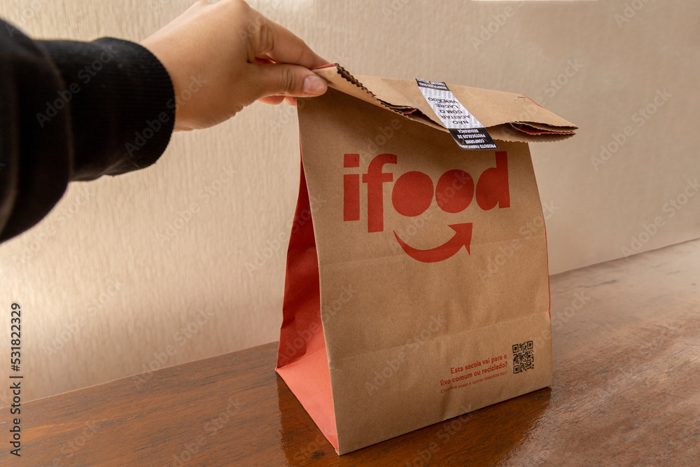 Foto de São Paulo, Brazil. August 20, 2022. Hand picking up ifood delivery  bag on wooden table. do Stock | Adobe Stock