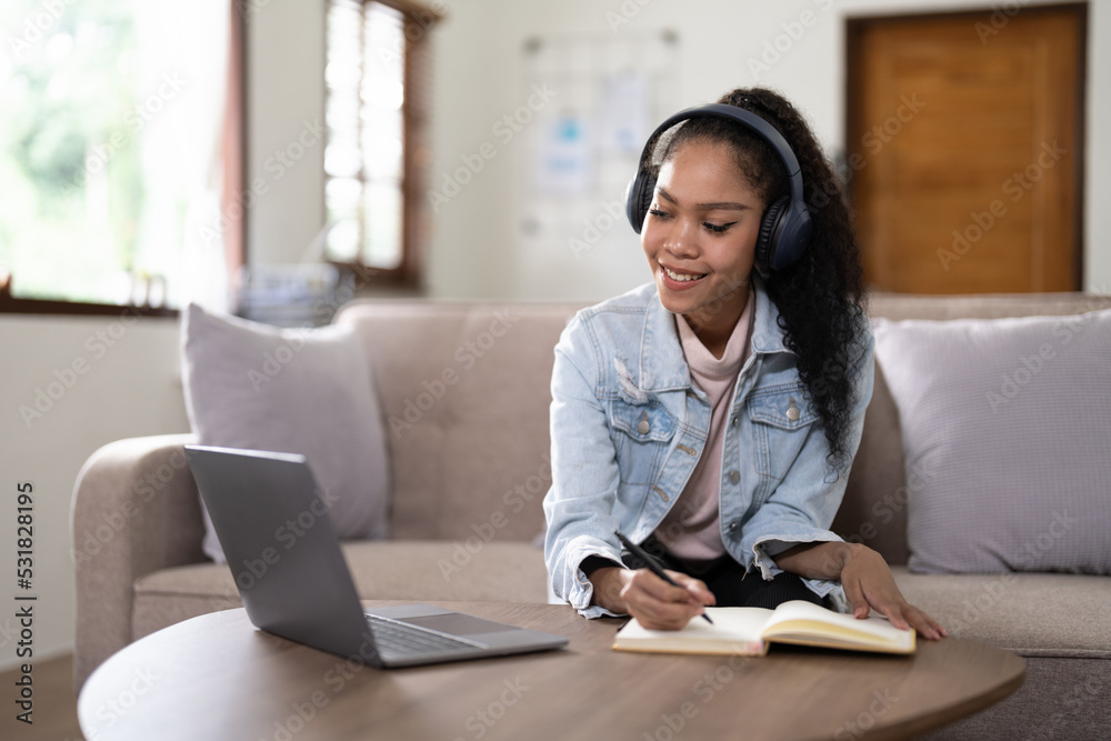 mixed race woman wearing headphones watching webinar write notes study online with online teacher, african female student learning language computer course on laptop listen translate lecture mixed race woman wearing headphones watching webinar write notes study online with online teacher, african female student learning language computer course on laptop listen translate lecture