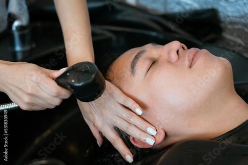 Directly above Asian male lying down for hair wash at hair salon with eyes closed